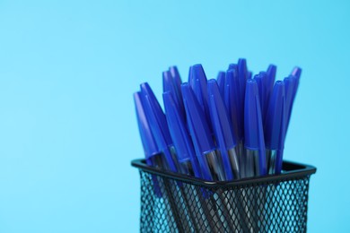 Photo of Many ballpoint pens in holder on light blue background, closeup. Space for text