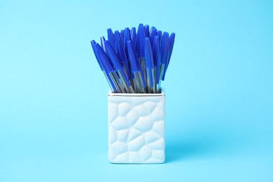 Photo of Many ballpoint pens in holder on light blue background