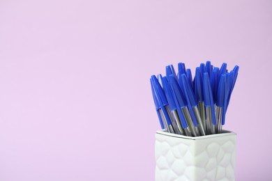 Photo of Many ballpoint pens in holder on pink background, closeup. Space for text