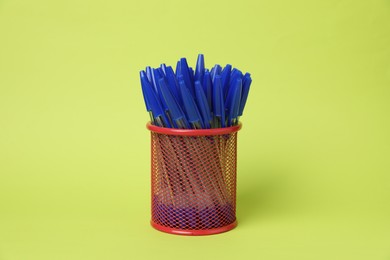 Photo of Many ballpoint pens in holder on green background