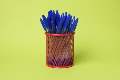 Photo of Many ballpoint pens in holder on green background