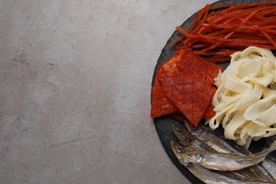 Photo of Many different dried fish snacks on grey table, top view. Space for text