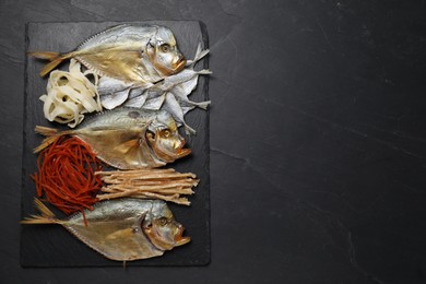 Many different dried fish snacks on black table, top view. Space for text