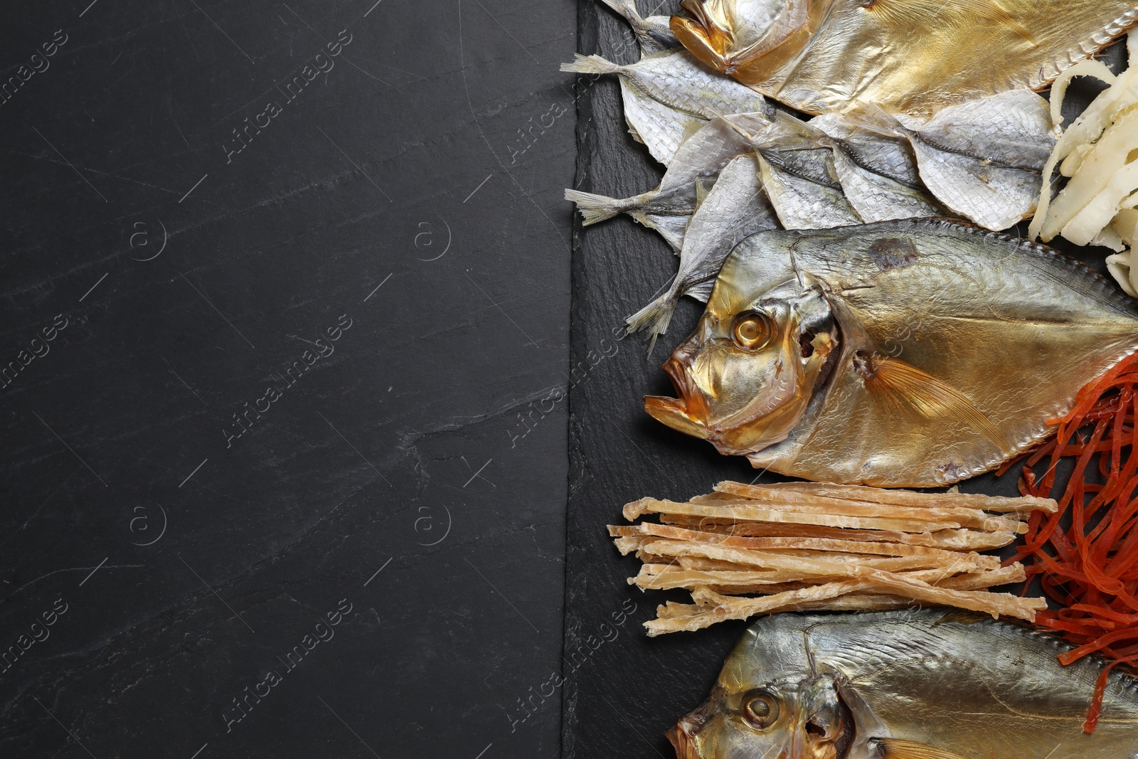 Photo of Many different dried fish snacks on black table, top view. Space for text