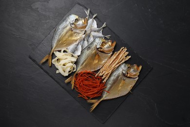 Many different dried fish snacks on black table, top view