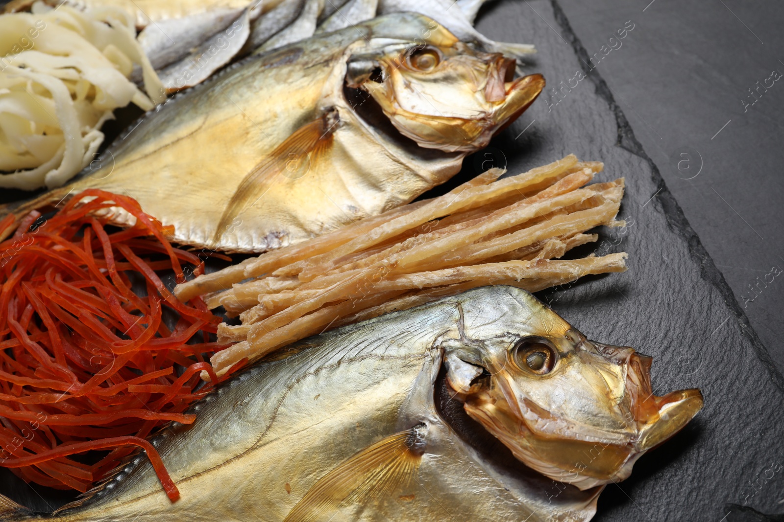 Photo of Many different dried fish snacks on black table, closeup