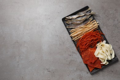 Photo of Many different dried fish snacks on grey table, top view. Space for text