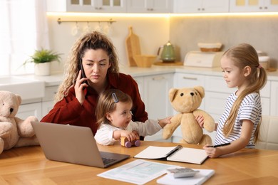 Work-family balance. Single mother talking on smartphone while her daughters playing at table in kitchen