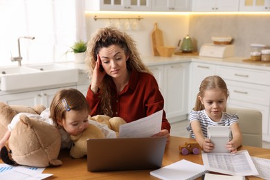 Photo of Work-family balance. Single mother with document and her daughters at table in kitchen