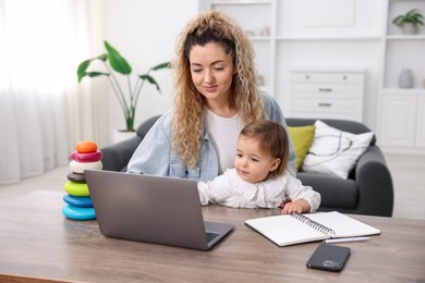 Photo of Single mother working with laptop and her daughter at table indoors