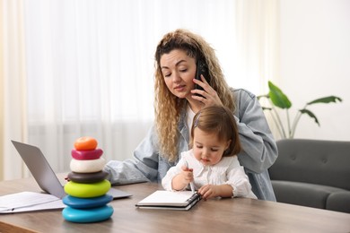 Work-family balance. Single mother talking on smartphone and her daughter at table indoors