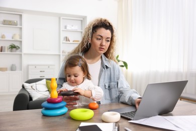 Photo of Single mother working with laptop and her daughter at table indoors