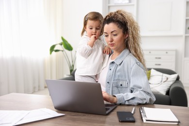 Photo of Single mother holding her daughter while working on laptop at table indoors