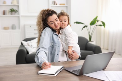 Photo of Single mother holding her daughter while talking on smartphone at table indoors