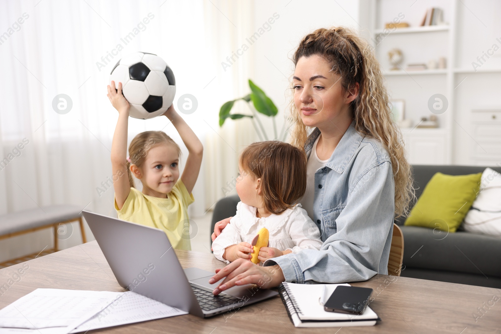 Photo of Single mother working at table while her daughters playing indoors