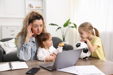 Photo of Single mother working at table while her daughters playing indoors