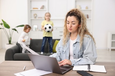 Photo of Single mother working at table while her daughters playing on sofa indoors, selective focus