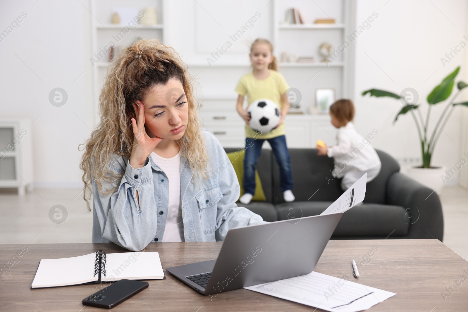 Photo of Single mother working at table while her daughters playing on sofa indoors, selective focus