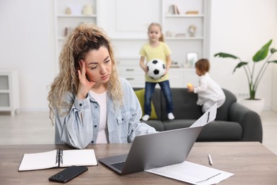 Single mother working at table while her daughters playing on sofa indoors, selective focus