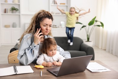 Work-family balance. Single mother holding daughter and talking on smartphone while her other child playing on sofa indoors, selective focus