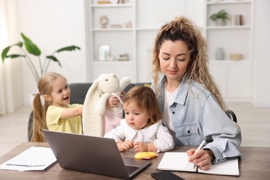 Photo of Work-family balance. Single mother taking notes and her daughters at table indoors