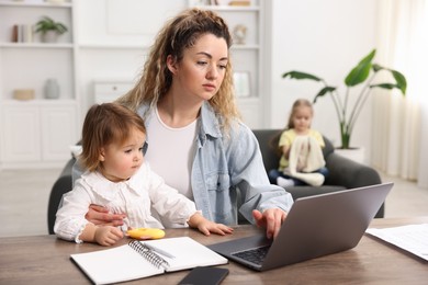 Photo of Single mother working with laptop at table and her daughters indoors, selective focus