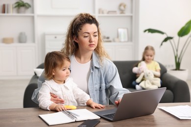 Photo of Single mother working with laptop at table and her daughters indoors, selective focus