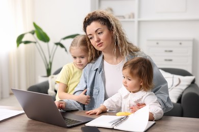 Photo of Single mother working with laptop and her daughters at table indoors