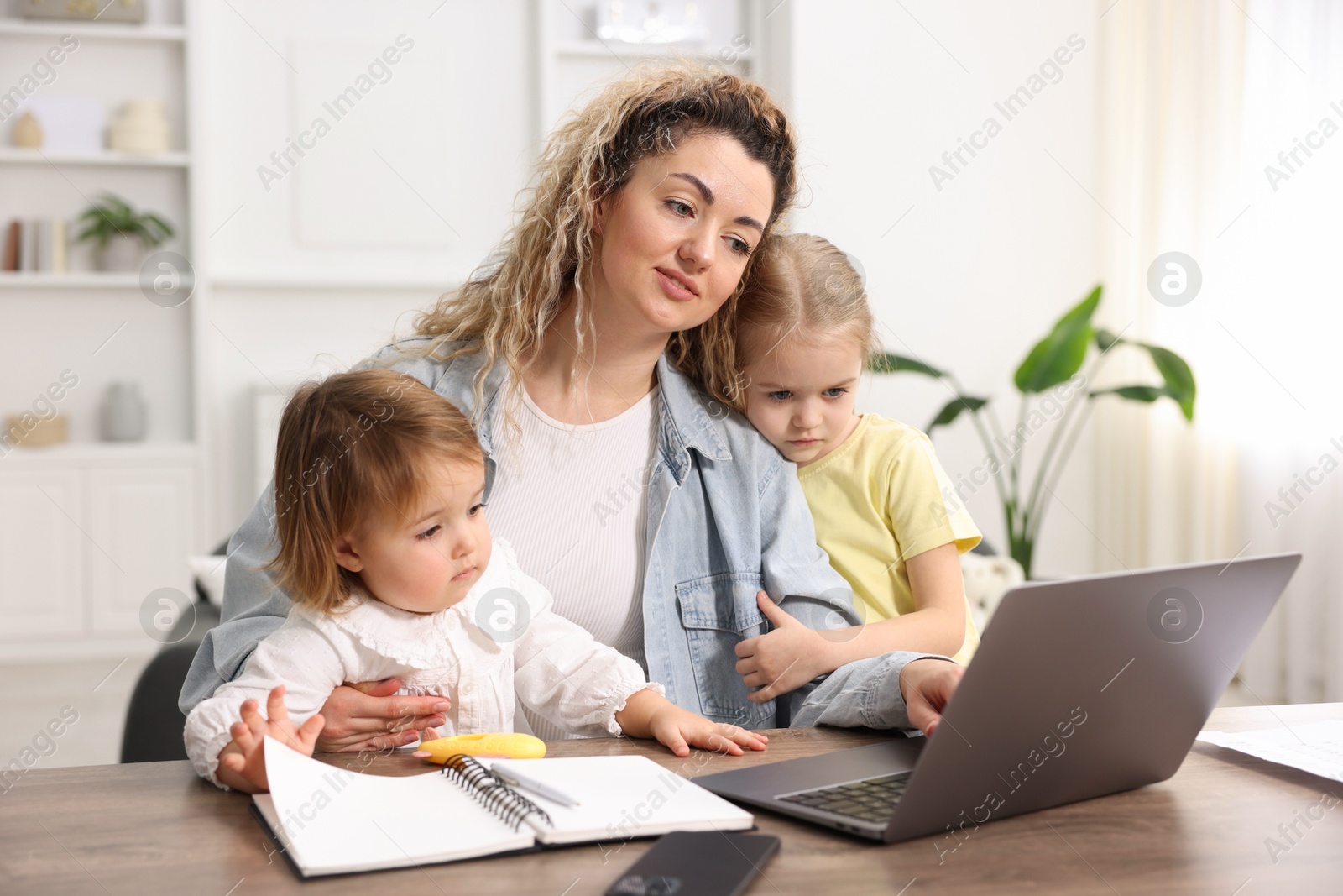 Photo of Single mother working with laptop and her daughters at table indoors