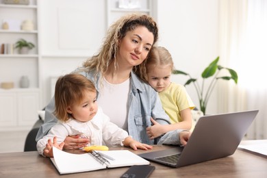 Single mother working with laptop and her daughters at table indoors