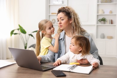 Photo of Single mother working with laptop and her daughters at table indoors