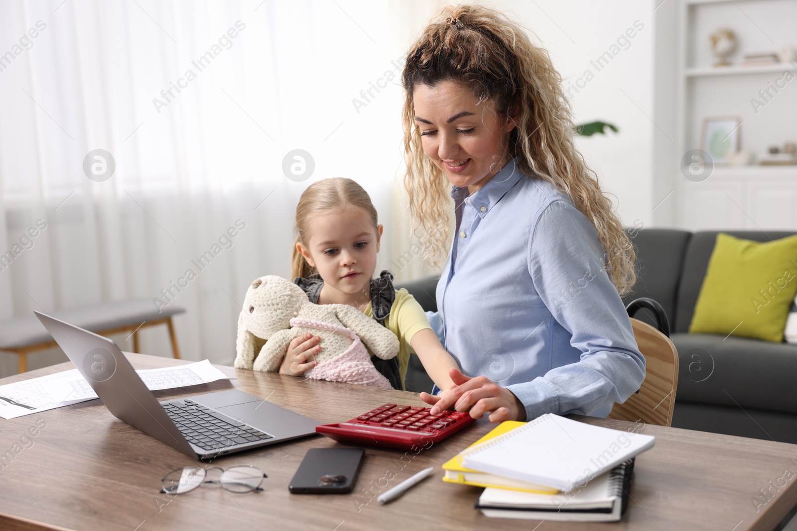 Photo of Work-family balance. Single mother using calculator and her daughter at table indoors