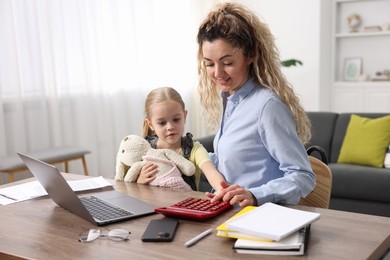 Work-family balance. Single mother using calculator and her daughter at table indoors