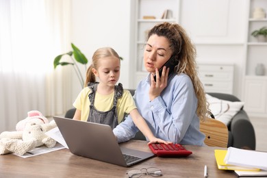 Work-family balance. Single mother talking on smartphone and her daughter at table indoors