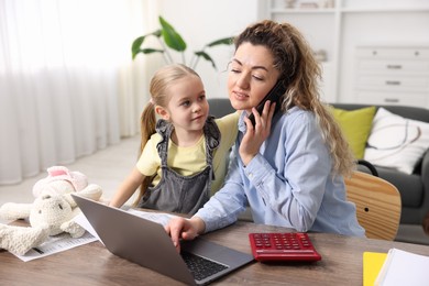 Work-family balance. Single mother talking on smartphone and her daughter at table indoors