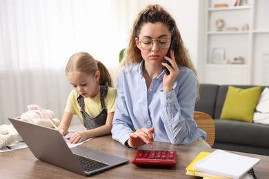 Work-family balance. Single mother using calculator while talking on smartphone and her daughter at table indoors