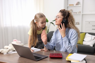 Photo of Work-family balance. Single mother talking on smartphone and her daughter at table indoors