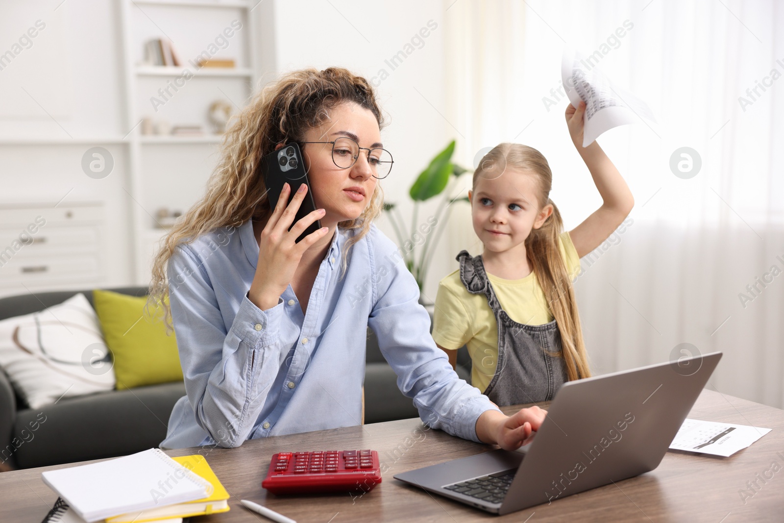 Photo of Work-family balance. Single mother talking on smartphone and her daughter at table indoors