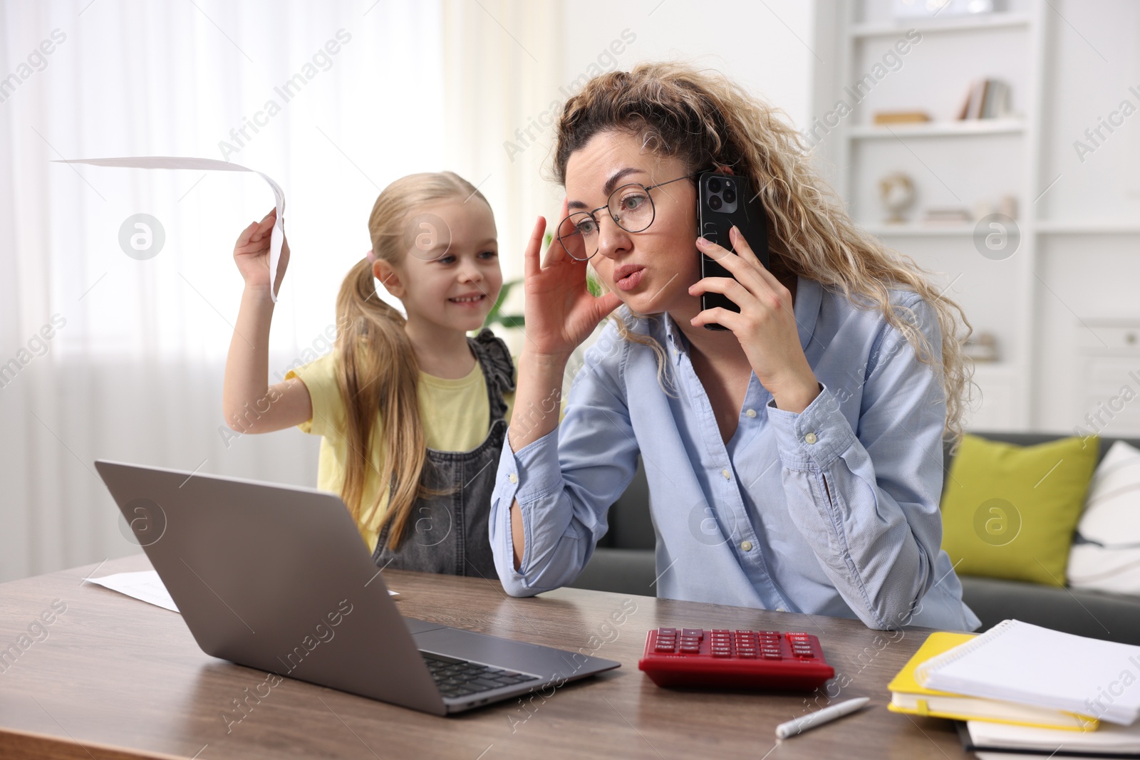 Photo of Work-family balance. Single mother talking on smartphone and her daughter at table indoors