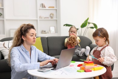 Photo of Single mother working on laptop while her daughters playing indoors