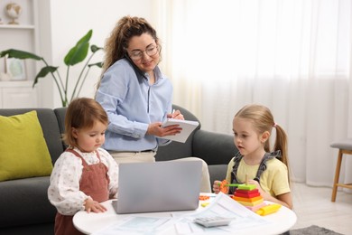 Photo of Work-family balance. Single mother taking notes while talking on smartphone and her daughters at home