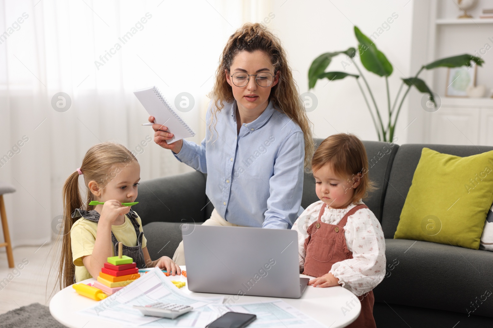 Photo of Work-family balance. Single mother with notebook and her daughters indoors