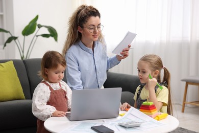 Photo of Work-family balance. Single mother with notebook and her daughters indoors