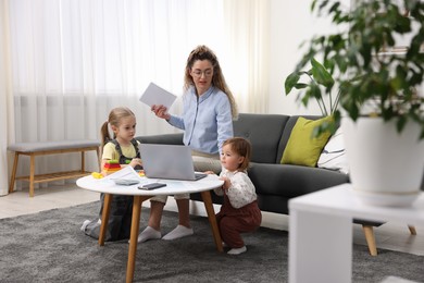 Work-family balance. Single mother with notebook and her daughters indoors