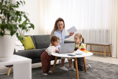 Photo of Work-family balance. Single mother with notebook and her daughters indoors