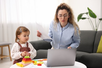 Photo of Work-family balance. Single mother with document and her daughter indoors