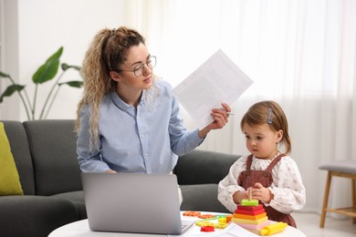 Photo of Work-family balance. Single mother with document and her daughter indoors