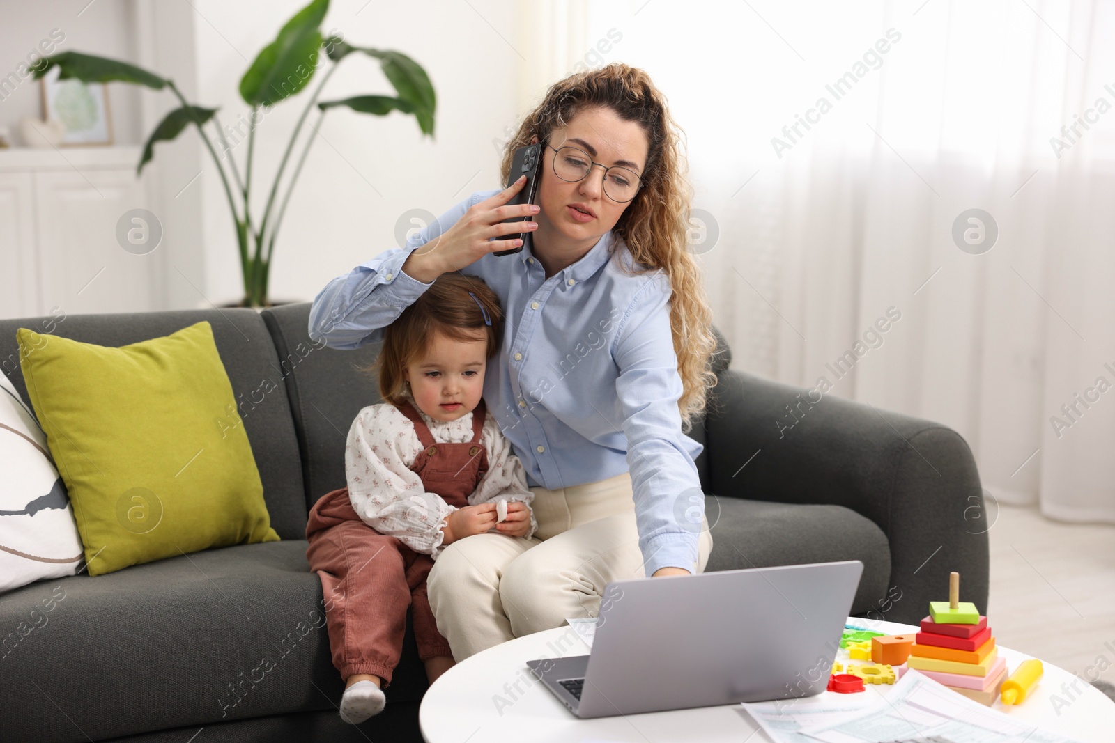 Photo of Work-family balance. Single mother talking on smartphone and her daughter indoors