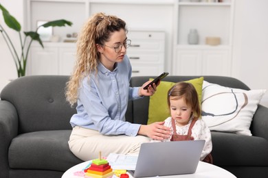 Photo of Work-family balance. Single mother with smartphone and her daughter indoors