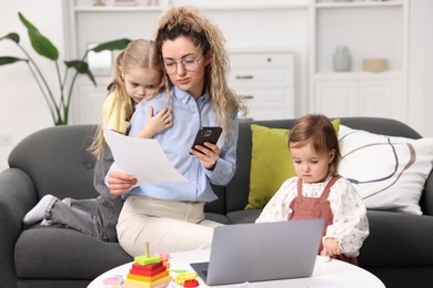 Photo of Work-family balance. Single mother with document using smartphone and her daughters indoors